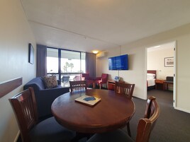 A hotel room with a dining area, a TV mounted on the wall, and a view of palm trees outside.