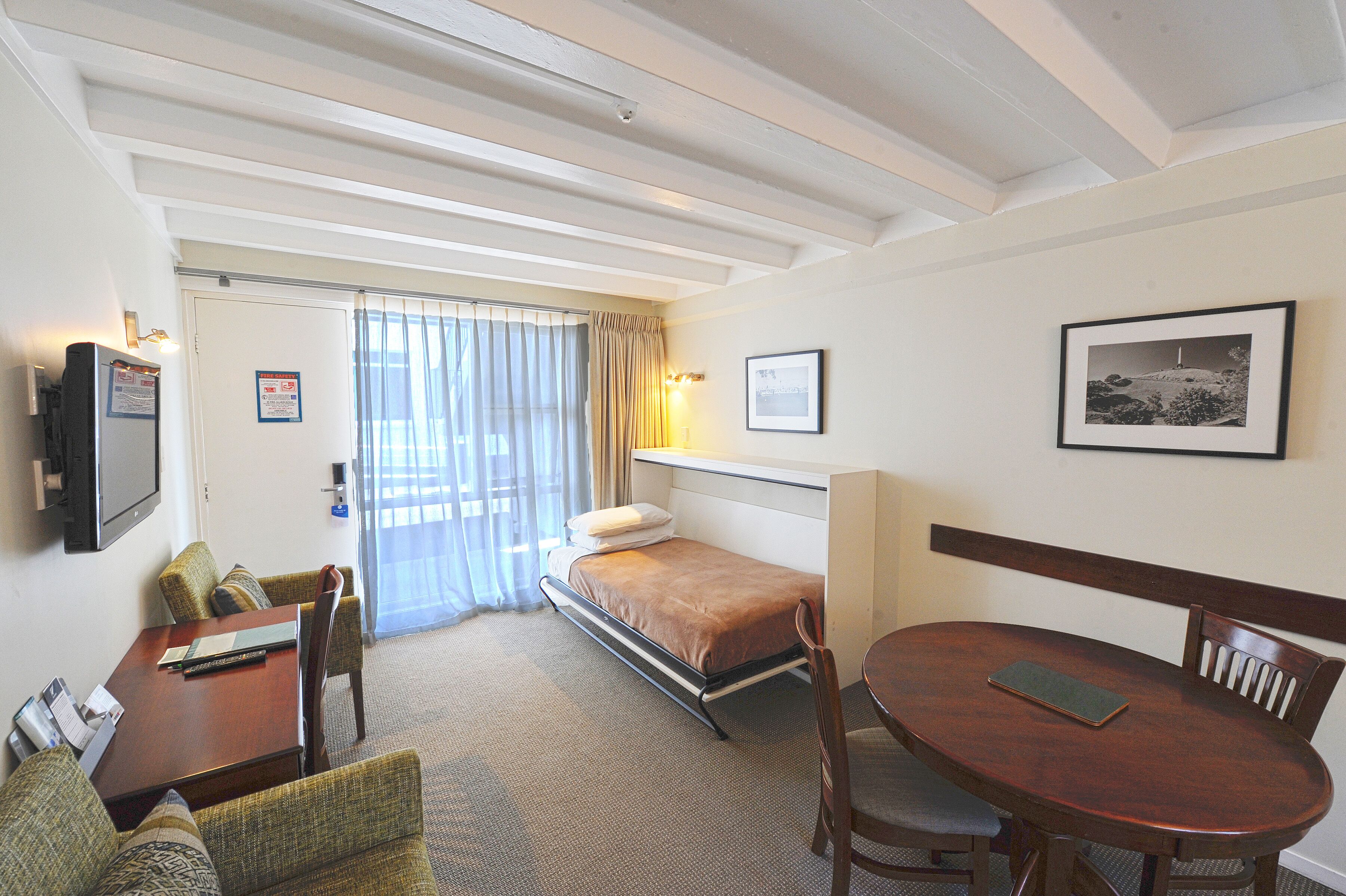 Habitación de hotel con una cama, un escritorio, una silla, un televisor y un cuadro en la pared.