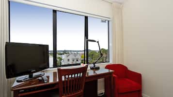 Una habitación de hotel con escritorio, televisor, una silla y un sillón rojo.