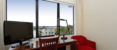 A hotel room with a desk, a television, a chair, and a red armchair.
