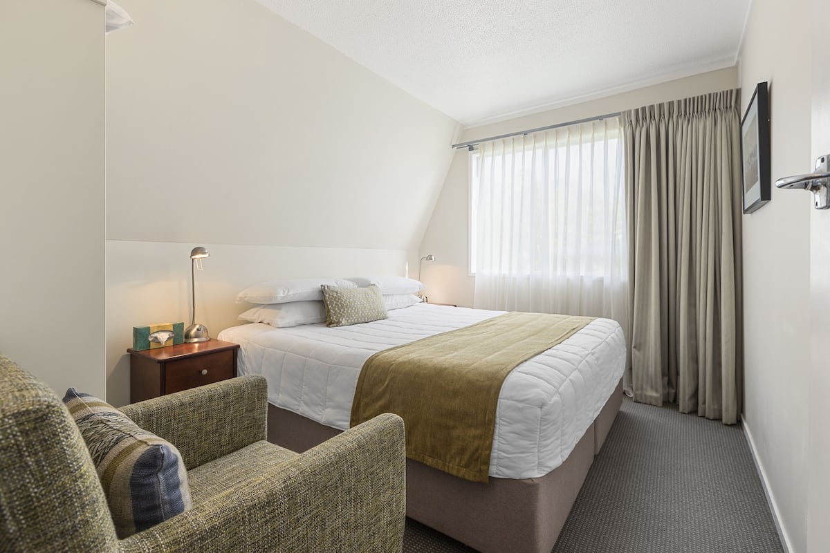 A hotel room with a bed, a nightstand, a chair, and a window with curtains.