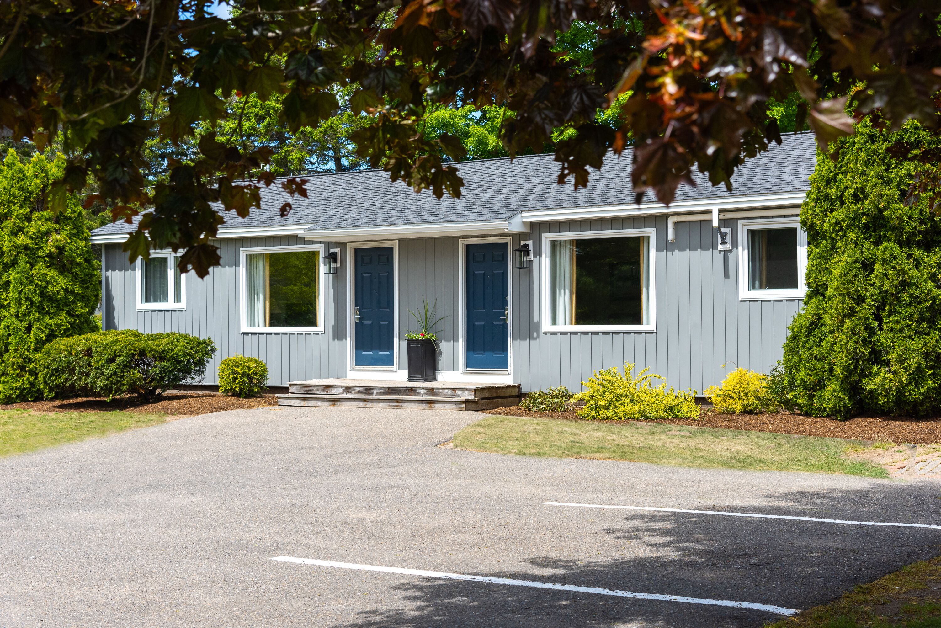 A two-story building with a grey exterior, a front entrance with a blue door, and a small front porch.
