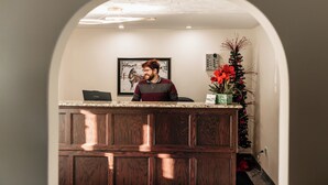 A reception desk with a framed picture on the wall, a small Christmas tree, and a vase with red flowers. - Aurora Inn (Kingston)