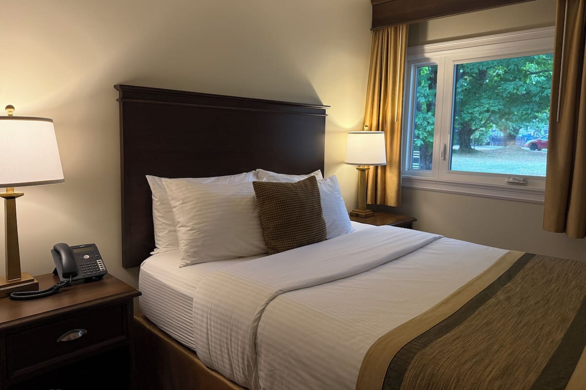 A hotel room with a large bed, two bedside lamps, a nightstand with a phone, and a window with curtains.