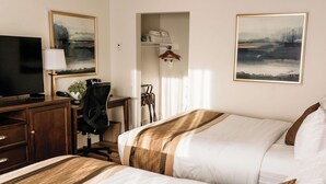 A hotel room with a bed, a desk with a computer, a TV, and a coat rack.