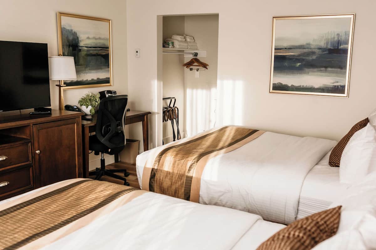 A hotel room with a bed, a desk with a computer, a TV, and a coat rack.