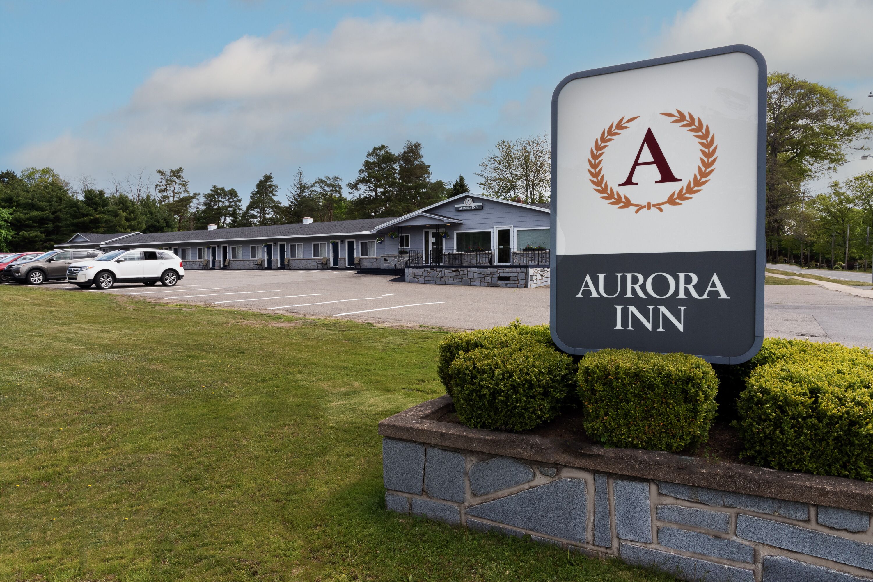 A sign for Aurora Inn with a parking lot and a building in the background.