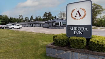 Señal de Aurora Inn, con un estacionamiento y un edificio al fondo.