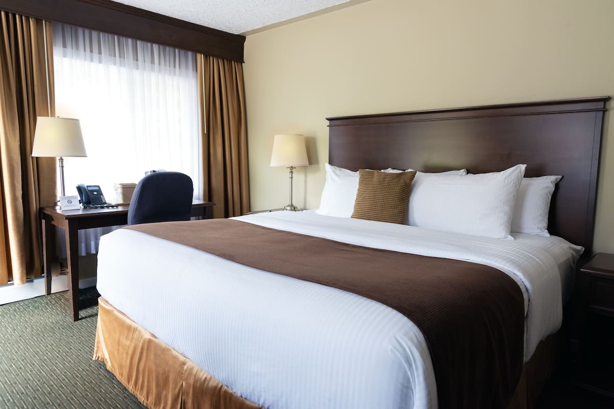 A hotel room with a large bed, two bedside lamps, a desk with a telephone, and a chair.