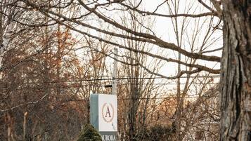 A sign with the letter 'A' and the name 'Aurora Inn' in a wooded area with bare trees and a snow-covered ground.
