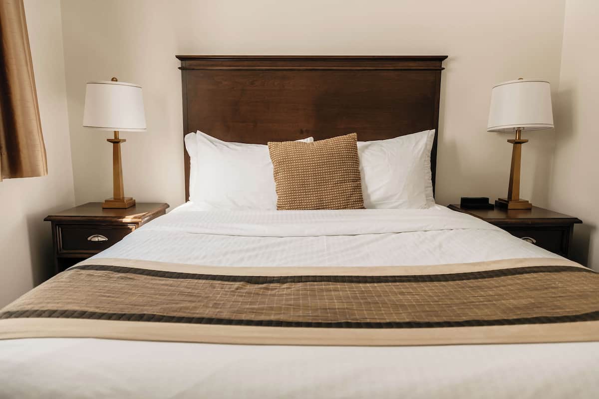 A neatly made bed with a wooden headboard, two bedside tables with lamps, and a brown woven throw pillow.