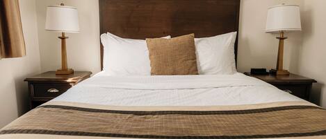 A neatly made bed with a wooden headboard, two bedside tables with lamps, and a brown woven throw pillow.