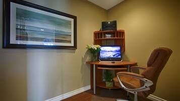 A home office setup with a laptop on a wooden desk, a framed picture on the wall, and a brown leather chair.