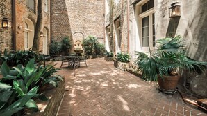 A courtyard with brick walls, potted plants, and a table with chairs. - French Market Inn (New Orleans)