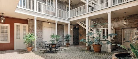 A courtyard with a brick floor, potted plants, a dining table with chairs, and a staircase.
