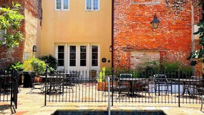 A swimming pool area with a brick building and a yellow building in the background. - French Market Inn (New Orleans)