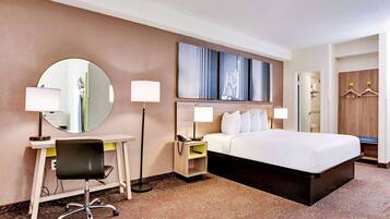 A hotel room with a bed, desk, chair, lamps, and a mirror.