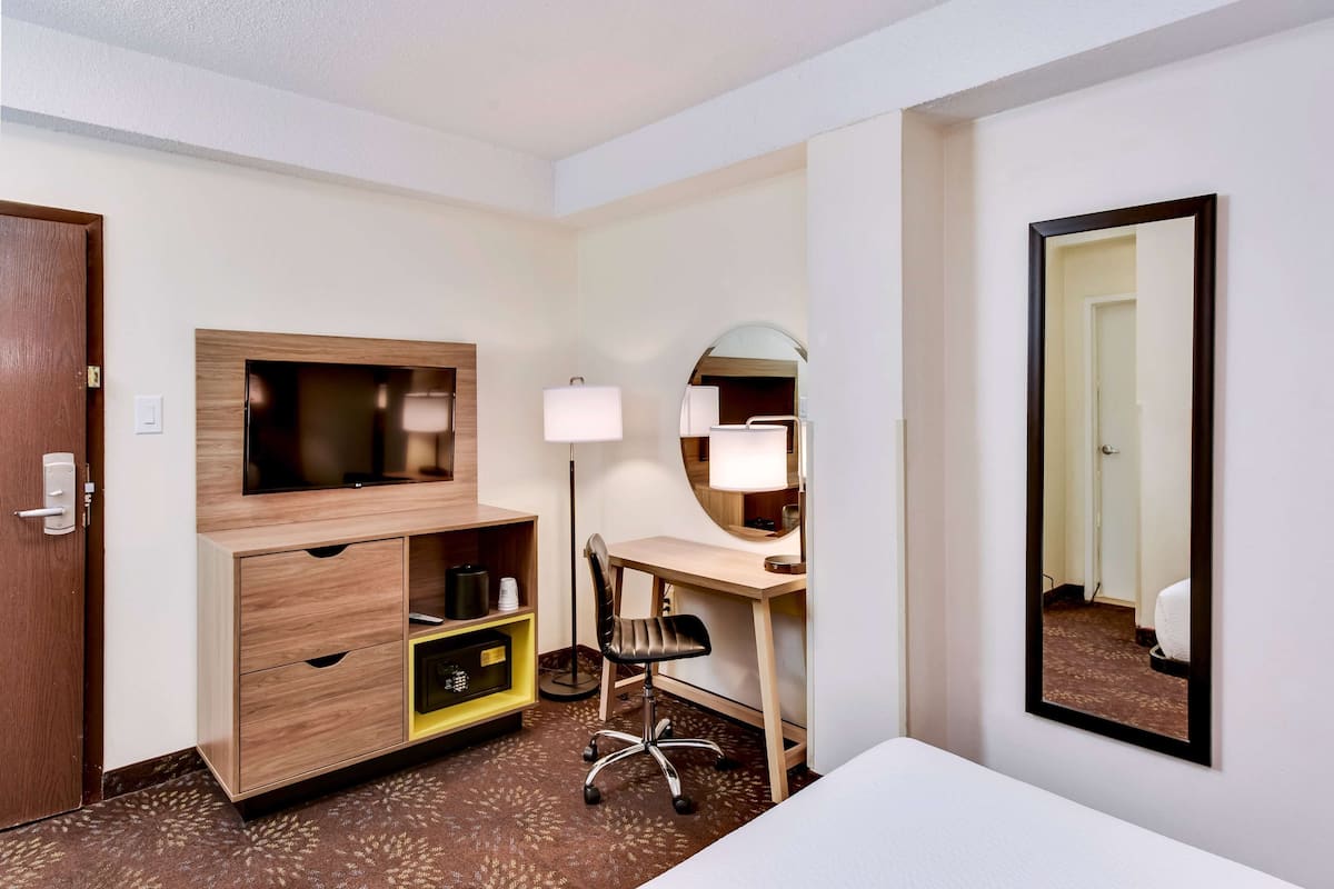 Una habitación de hotel con un escritorio de madera, una silla, un televisor, un espejo y un armario.