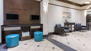 Um hall de entrada com balcão de recepção, duas televisões, área de estar com cadeiras e uma mesa de centro.