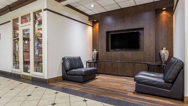 Um hall com piso de madeira, dois sofás de couro, uma TV fixada na parede e uma loja com fachada de vidro.