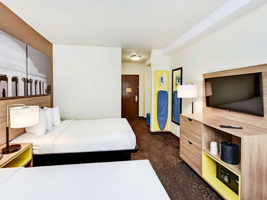A hotel room with two beds, a TV, a desk with a lamp, and a painting on the wall.
