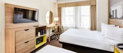A hotel room with a bed, a desk with a chair, a television, and a window with curtains.