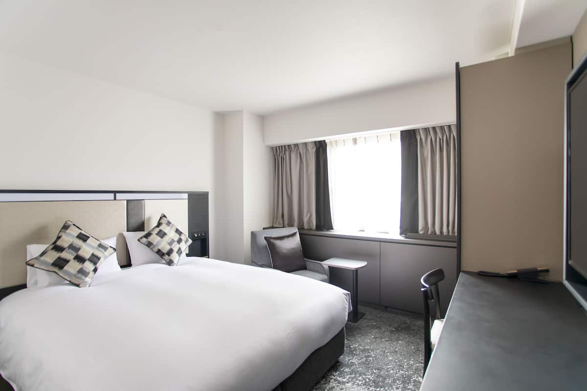 A hotel room with a large bed, a desk, a chair, and a TV.
