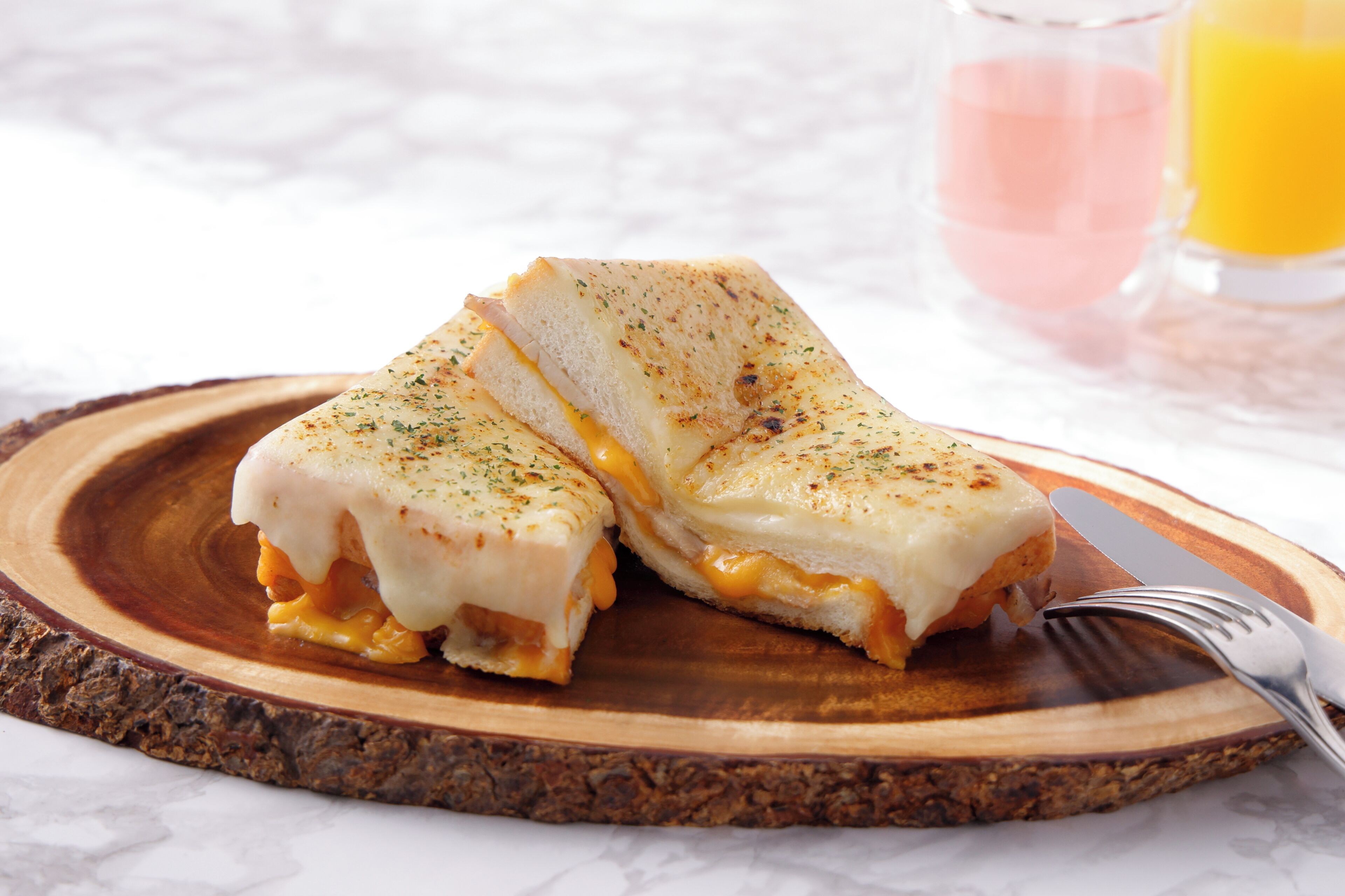 Un sándwich de queso a la plancha sobre una tabla de madera, con un tenedor al lado.