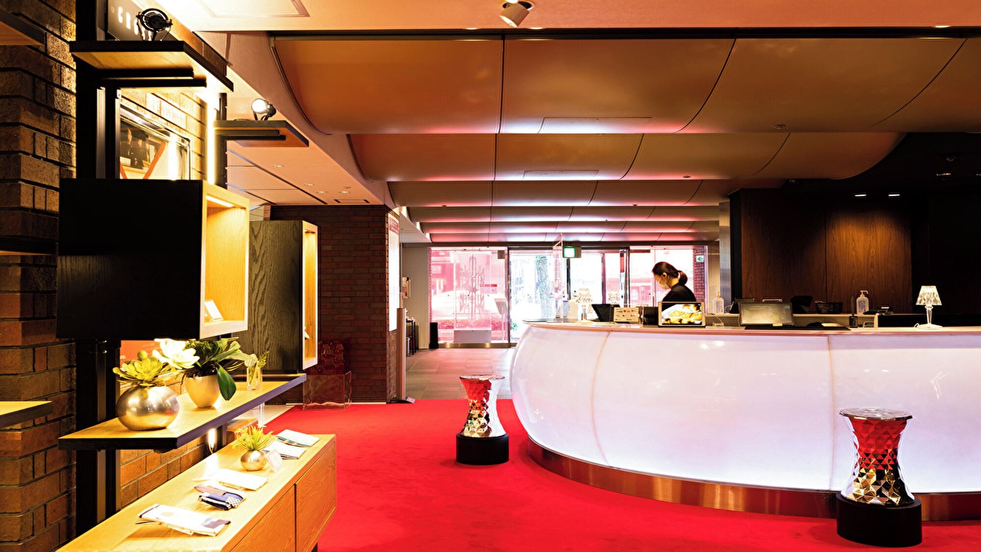 A reception area with a curved counter, a woman at the desk, and a red carpet.