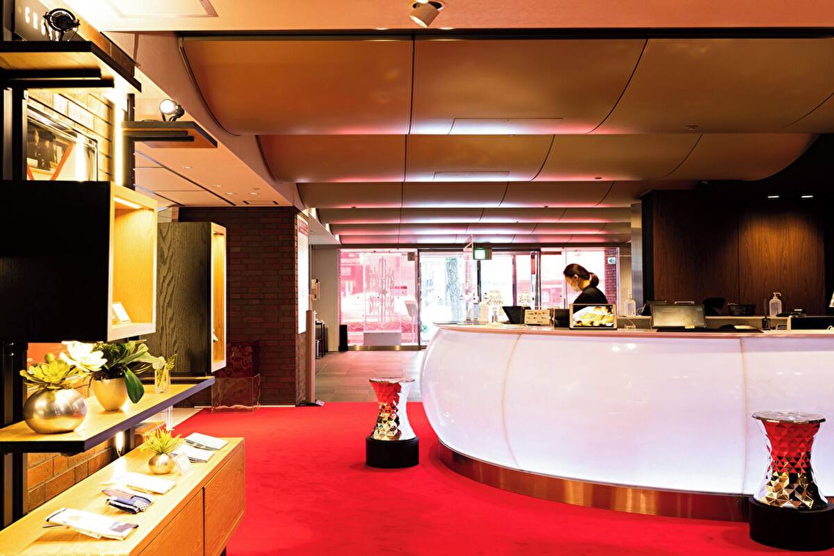 A reception area with a curved counter, a woman at the desk, and a red carpet.