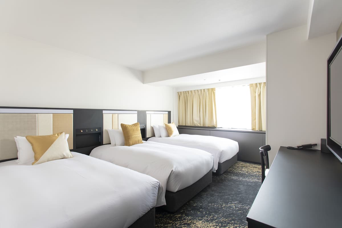 A hotel room with three beds, a desk, and a large window with curtains.