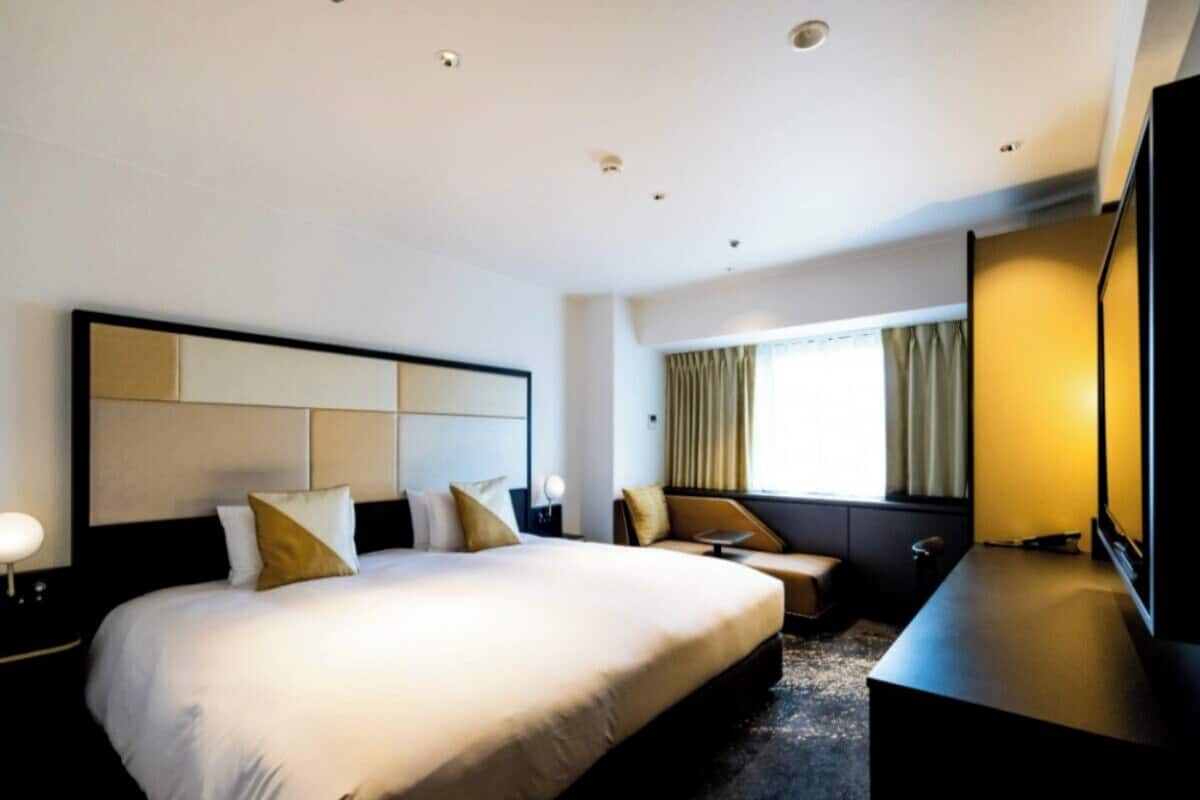 A modern hotel room with a large bed, a desk, a chair, and a TV.