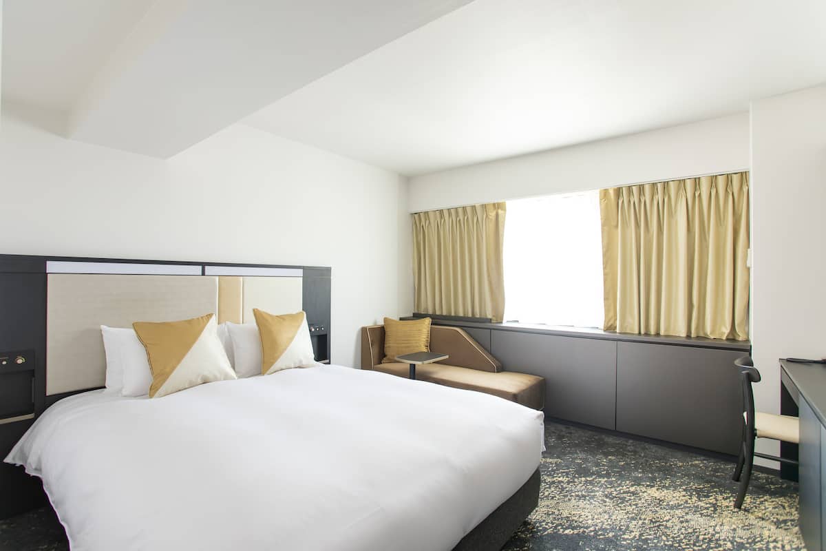 A hotel room with a large bed, a desk, a chair, and a window with curtains.