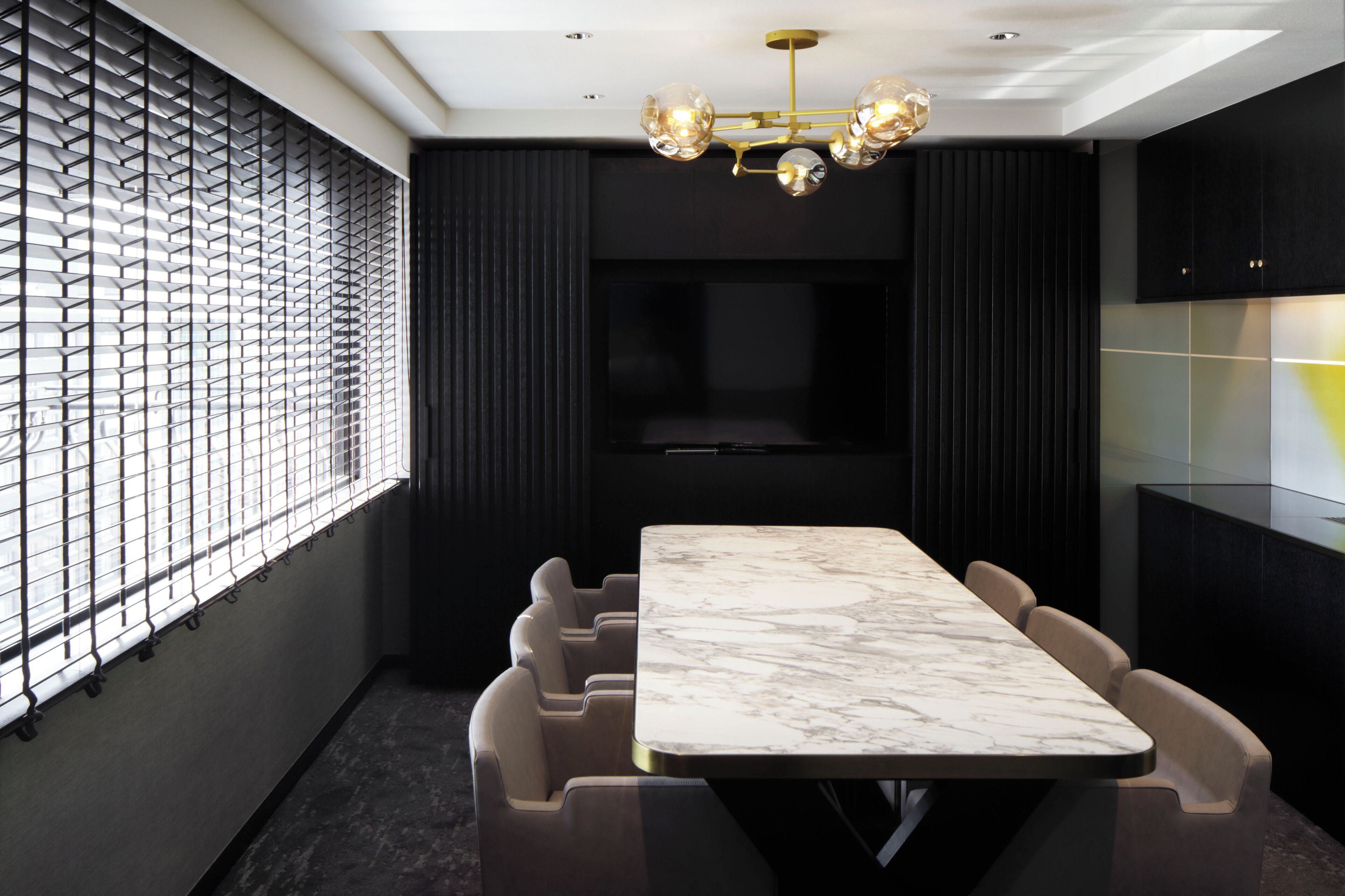 A modern dining area with a marble table and cushioned chairs, a black partition with a geometric pattern, and a ceiling light fixture.