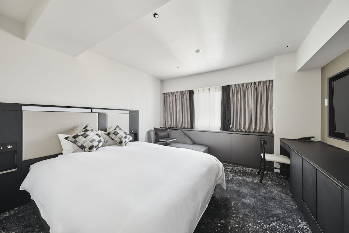 A modern hotel room with a large bed, a desk, and a TV.