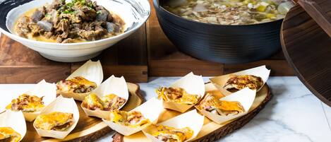 A wooden serving board with a bowl of soup, a pot of soup, and several pieces of food on bread.