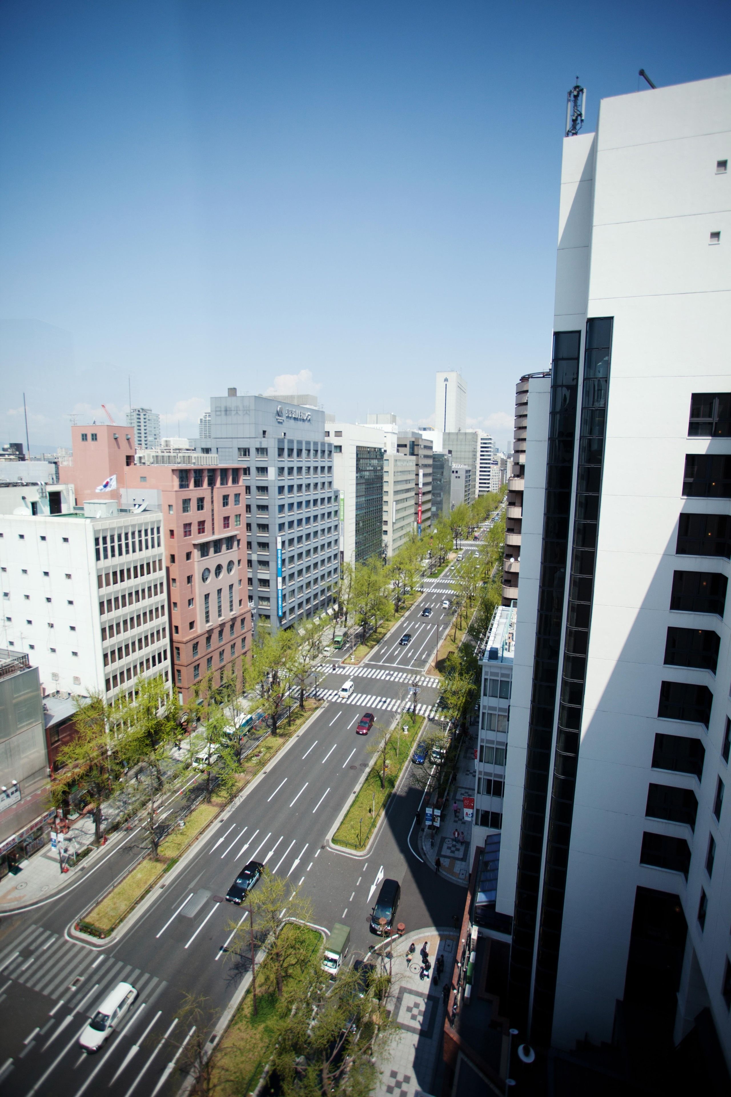 Un paysage urbain avec des bâtiments modernes, un ciel dégagé et une large route où circulent des véhicules.