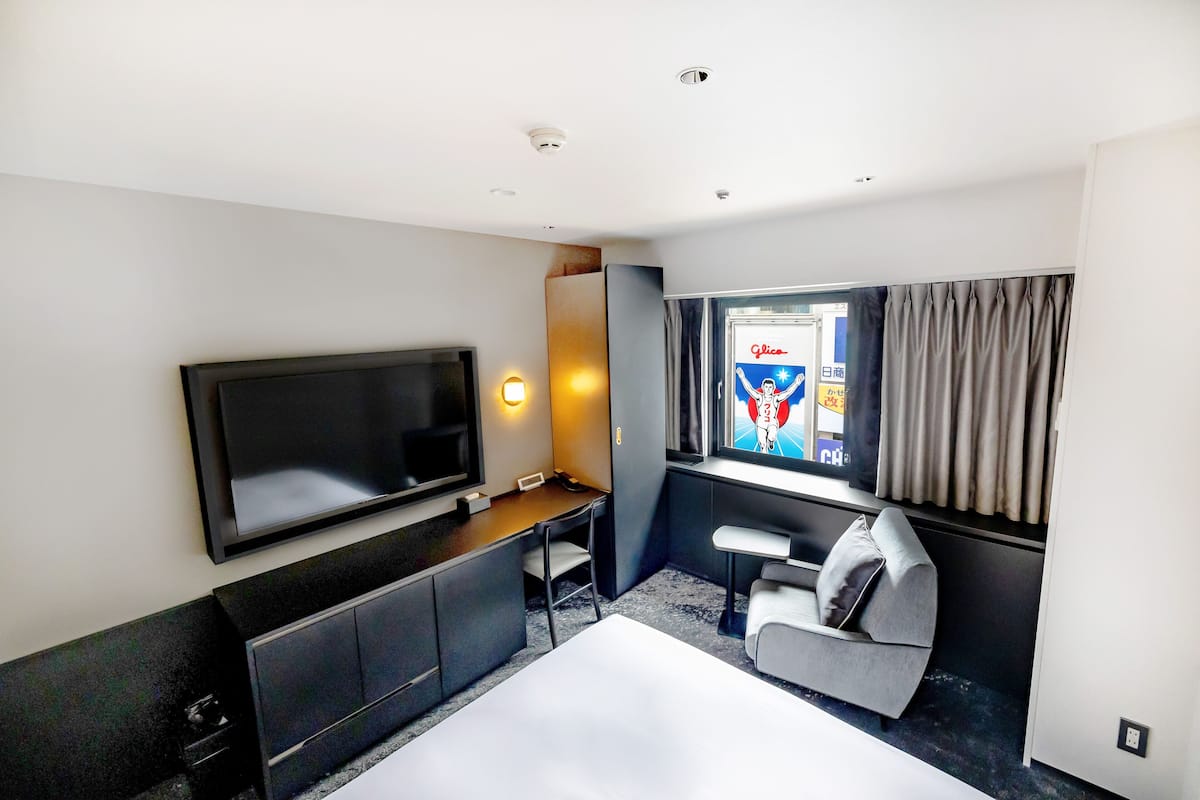 A modern hotel room with a flat-screen TV, a desk, a chair, and a sofa.