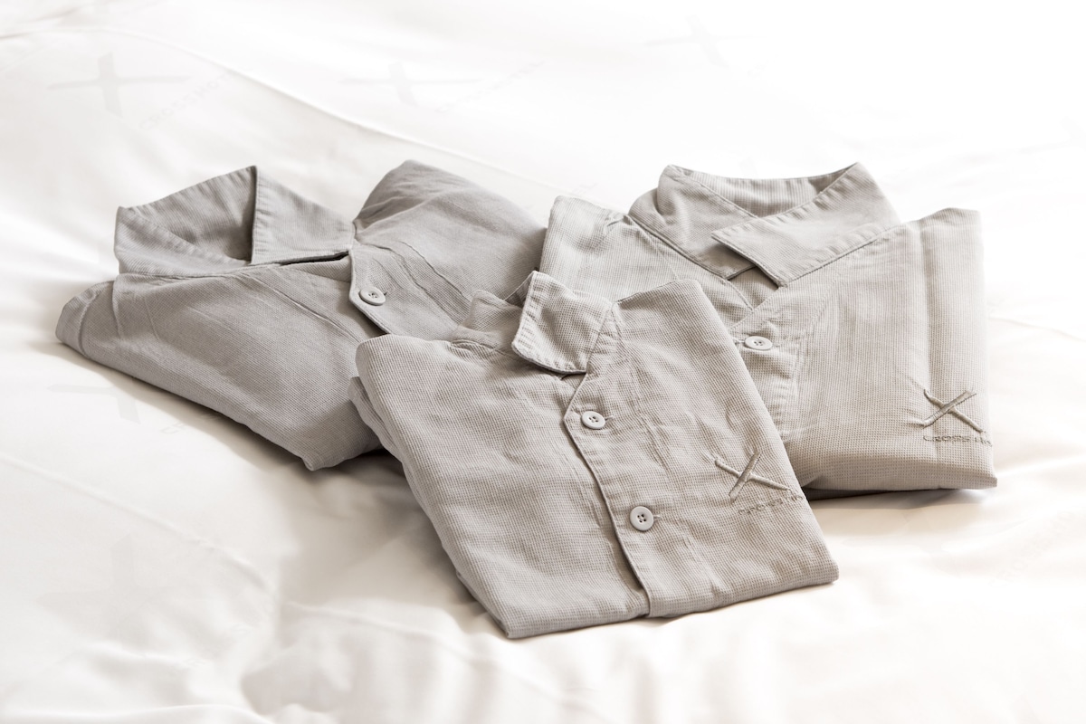 A neatly folded light-colored shirt on a bed with a white sheet.