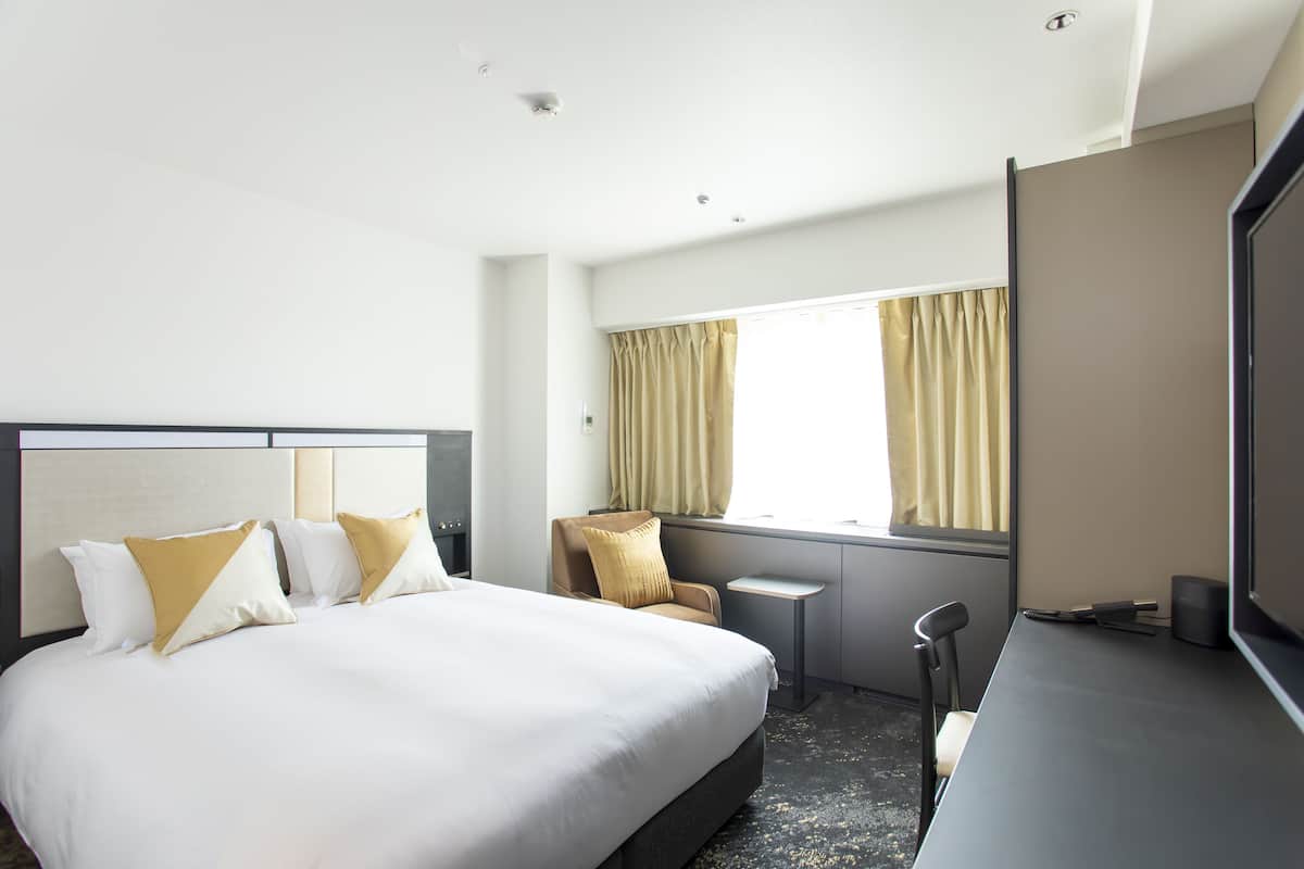 A hotel room with a large bed, a desk, a chair, a small table, and a TV.