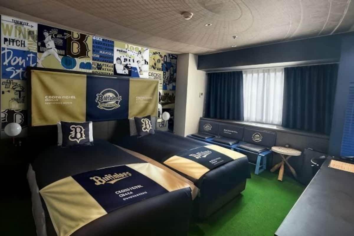 A hotel room with two beds, a desk, a small table, and a window with curtains.
