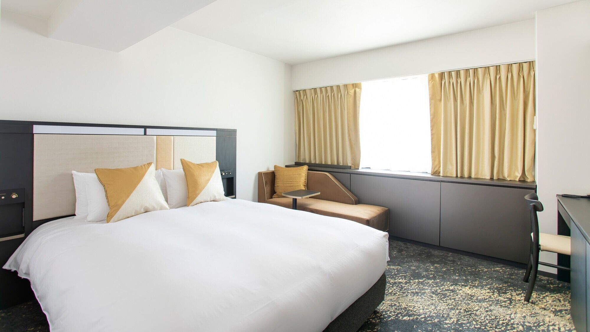 A hotel room with a large bed, a chair, a desk, and a window with curtains.