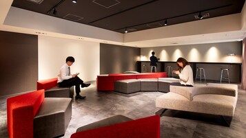A modern waiting area with red and grey seating, a laptop on a stool, and a person using a smartphone.