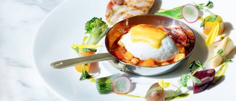 A white plate with a bowl of soup, a piece of meat, and various vegetables.