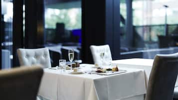 A dining table set with plates, glasses, and cutlery in a modern restaurant with large windows.