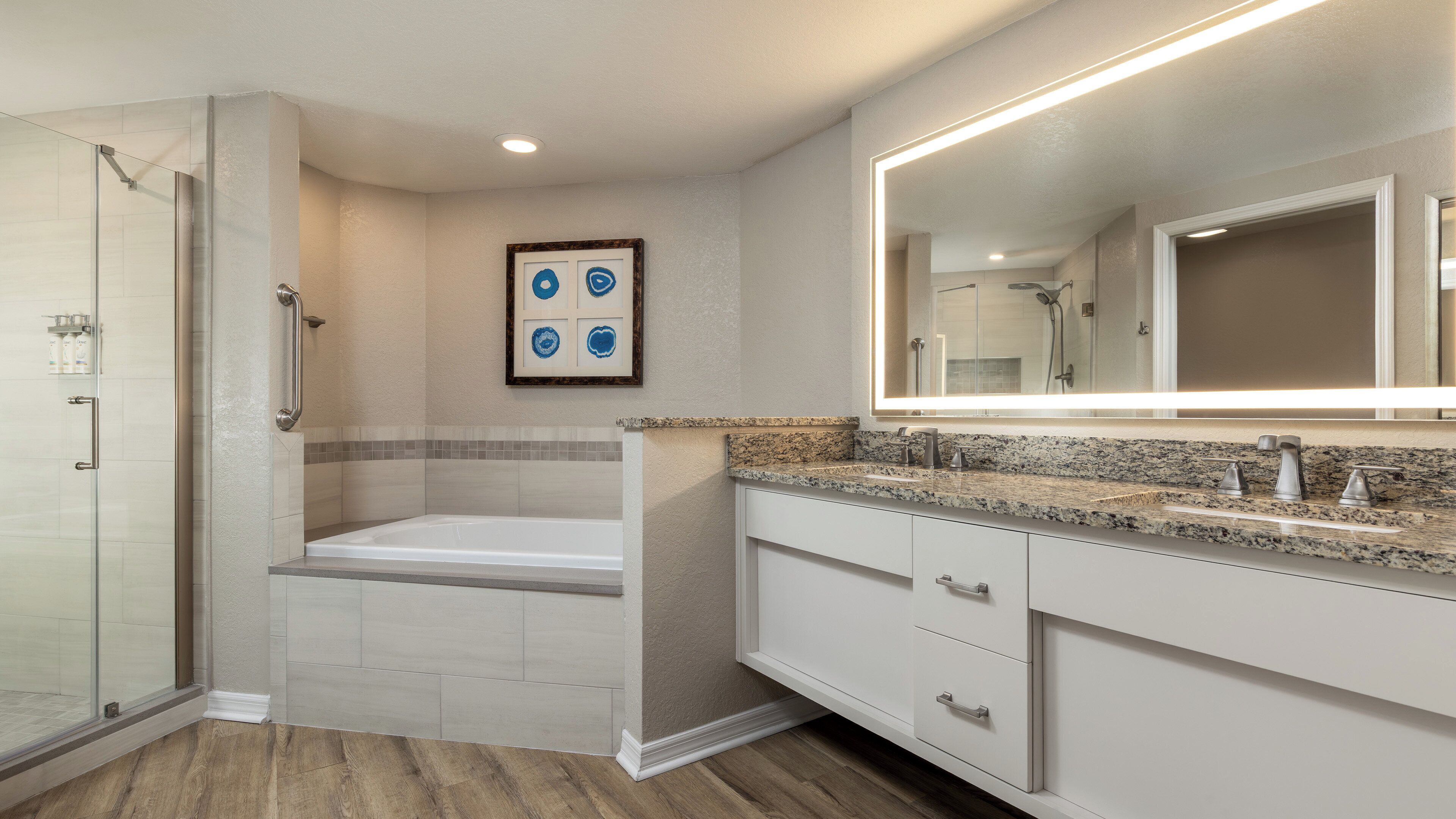 Un baño con cabina de ducha, bañera, espejo grande y tocador con encimera de granito.