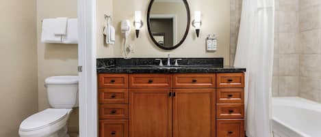 A bathroom with a toilet, sink, vanity with wooden cabinets, a mirror, and a shower curtain.