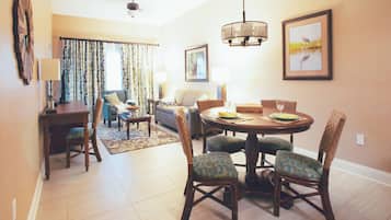 A dining area with a round table, chairs, and a chandelier. There is a sofa and a dining table in the background.