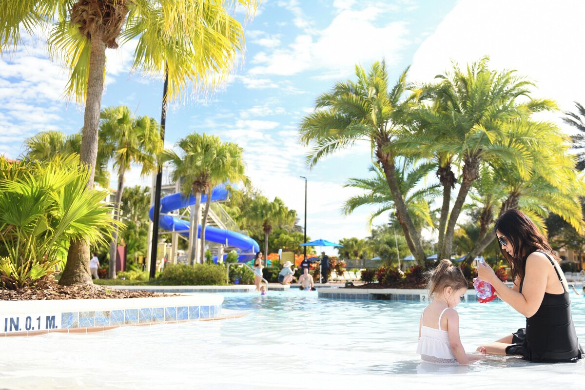 A pool area with palm trees, a water slide, and a lifeguard tower.
