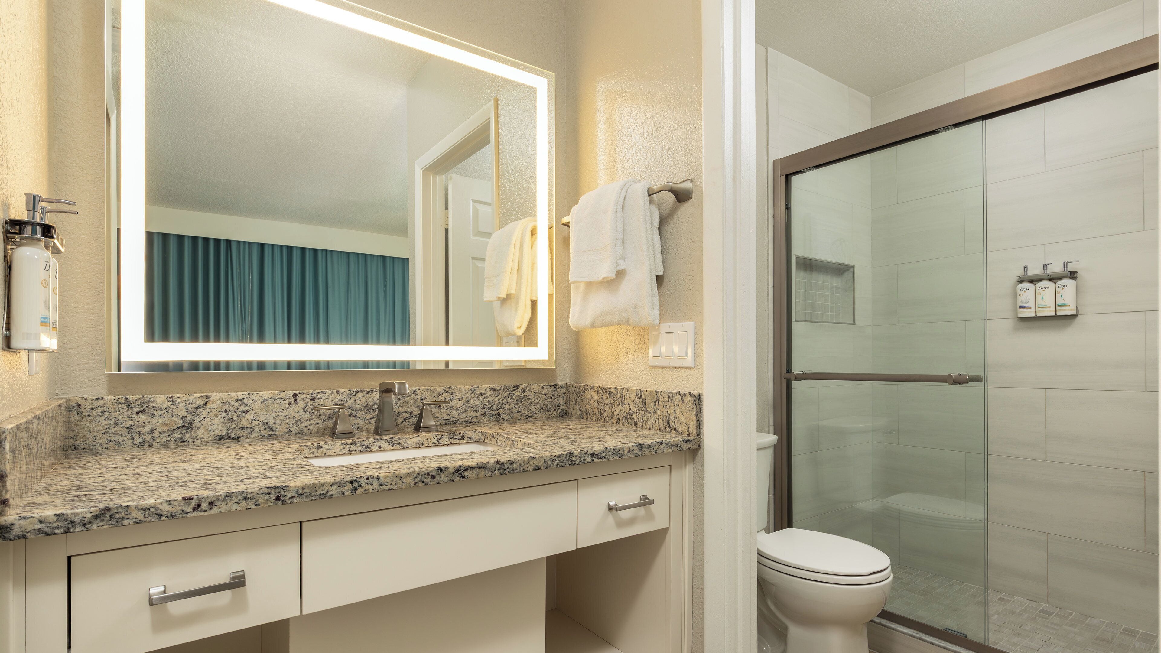 A bathroom with a granite countertop, a sink, a mirror, a towel rack, and a glass shower enclosure.